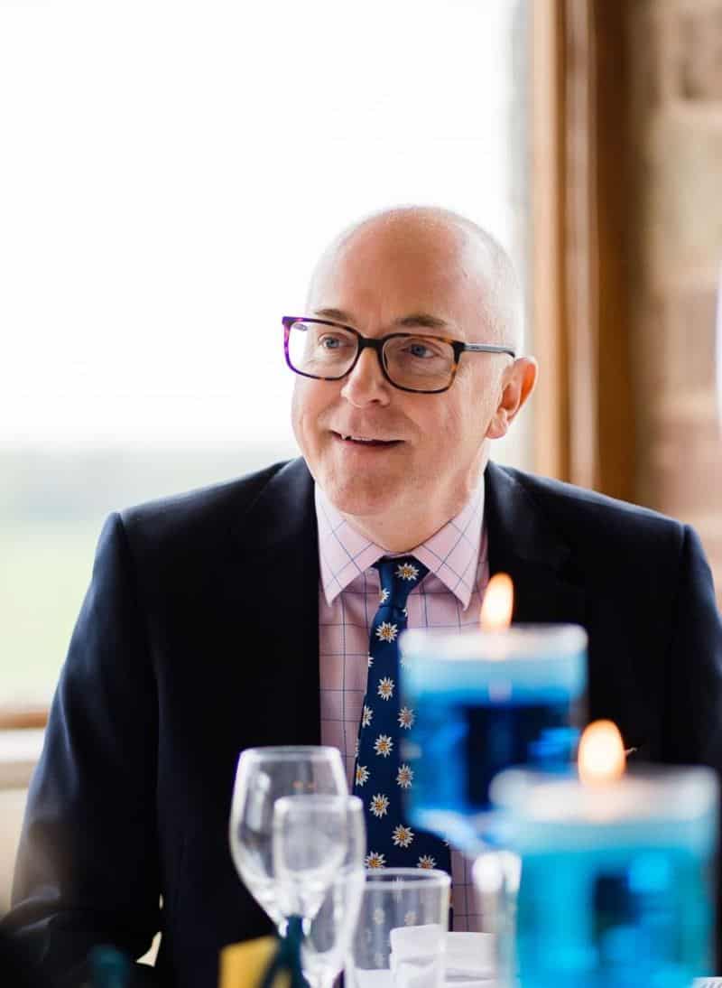 Patrick Tiley today, smiling in a navy suit and patterned tie